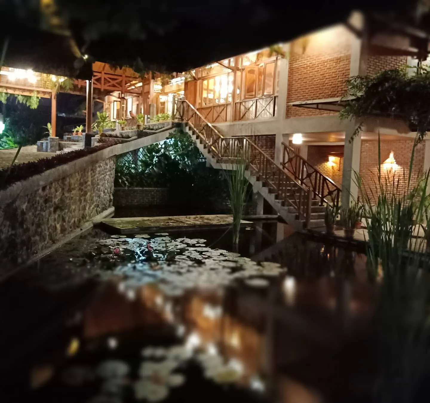 Lentera menyala di antara bungalow beratap ijuk, terpantul di kolam teratai pada malam hari